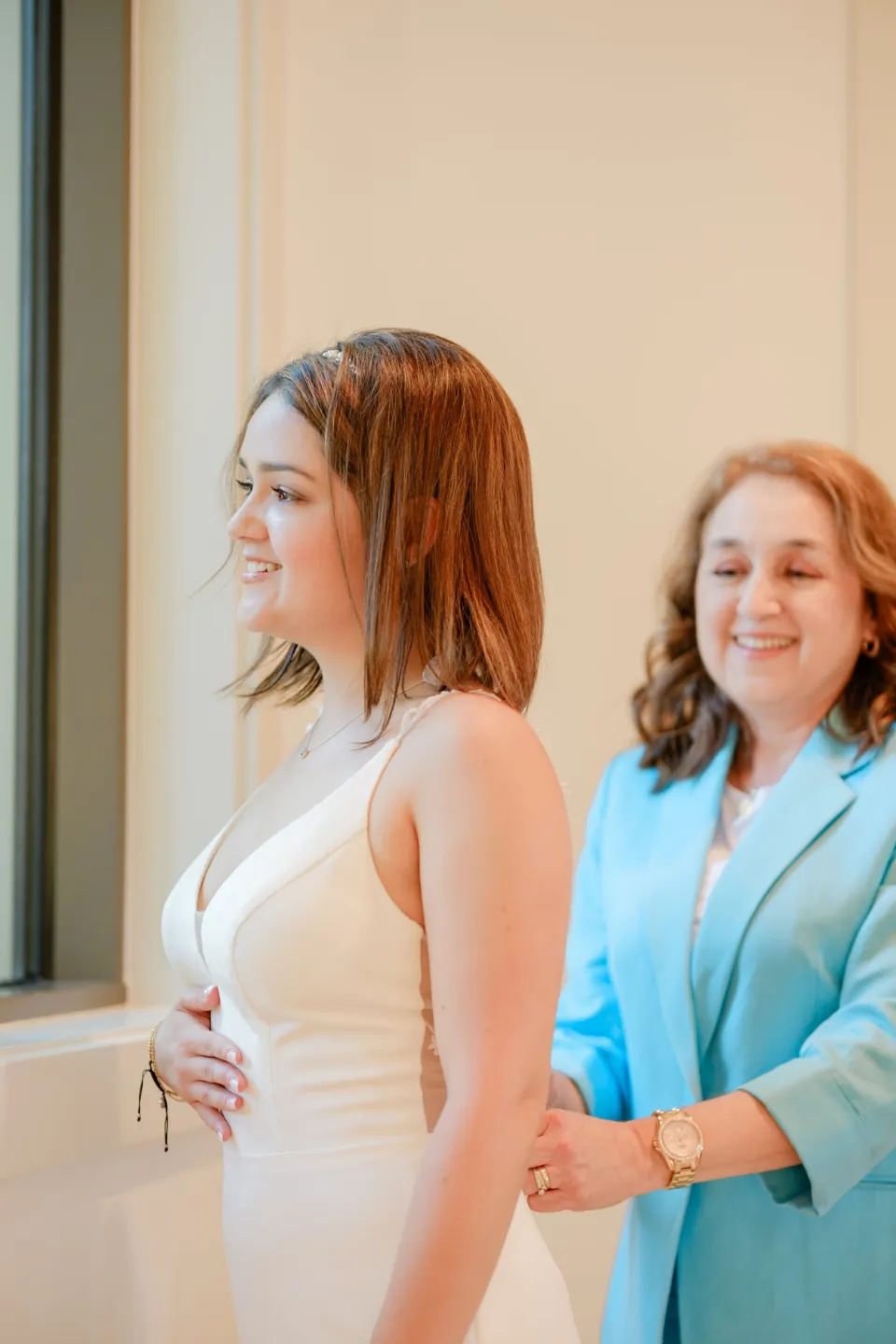 Bride and her mother by a sunlit window on the wedding morning
