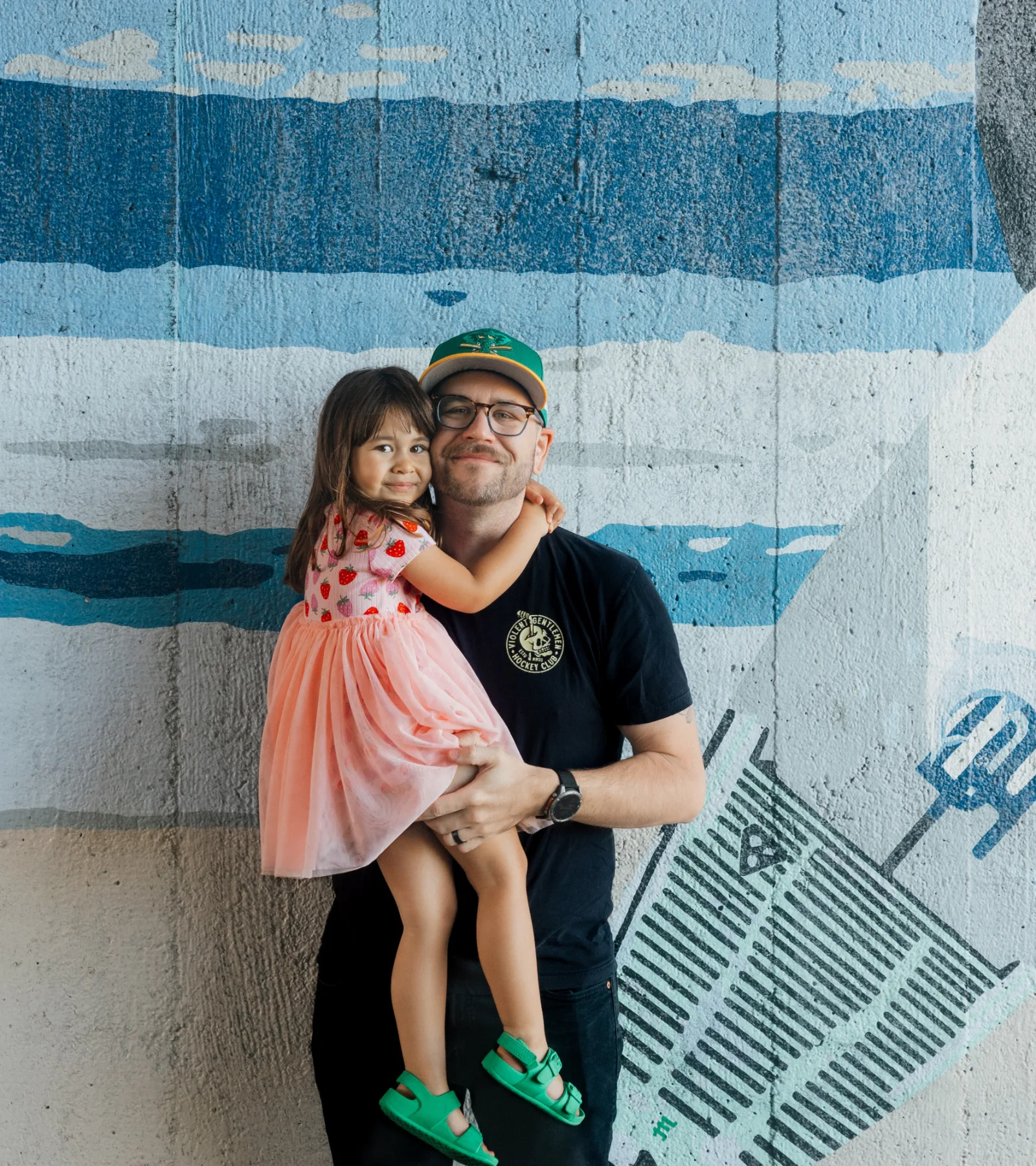 Dylan Andersen holding his daughter Alba in front of a painted mural