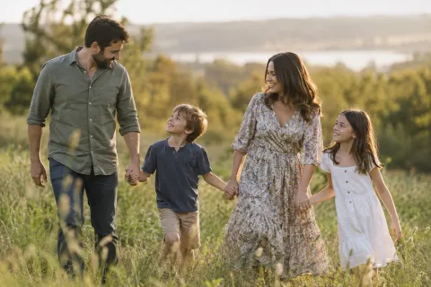 A family of four walking hand in hand through a meadow