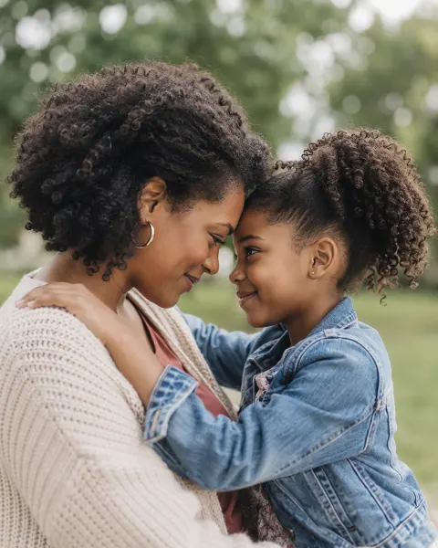A mother and daughter resting their foreheads together in a park
