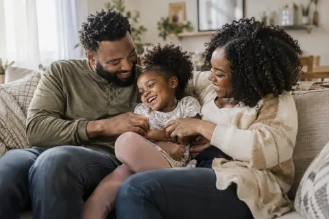 Parents laughing with their young child on a linen sofa
