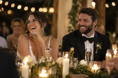 A bride and groom laughing during a toast at a candlelit reception