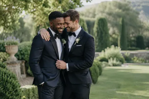 Two grooms embracing in a leafy estate garden